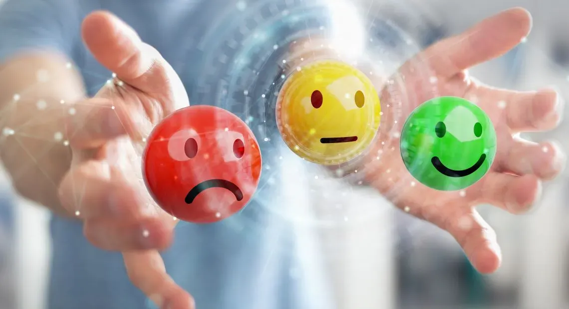 Hand holding red, yellow, and green smiley face ratings