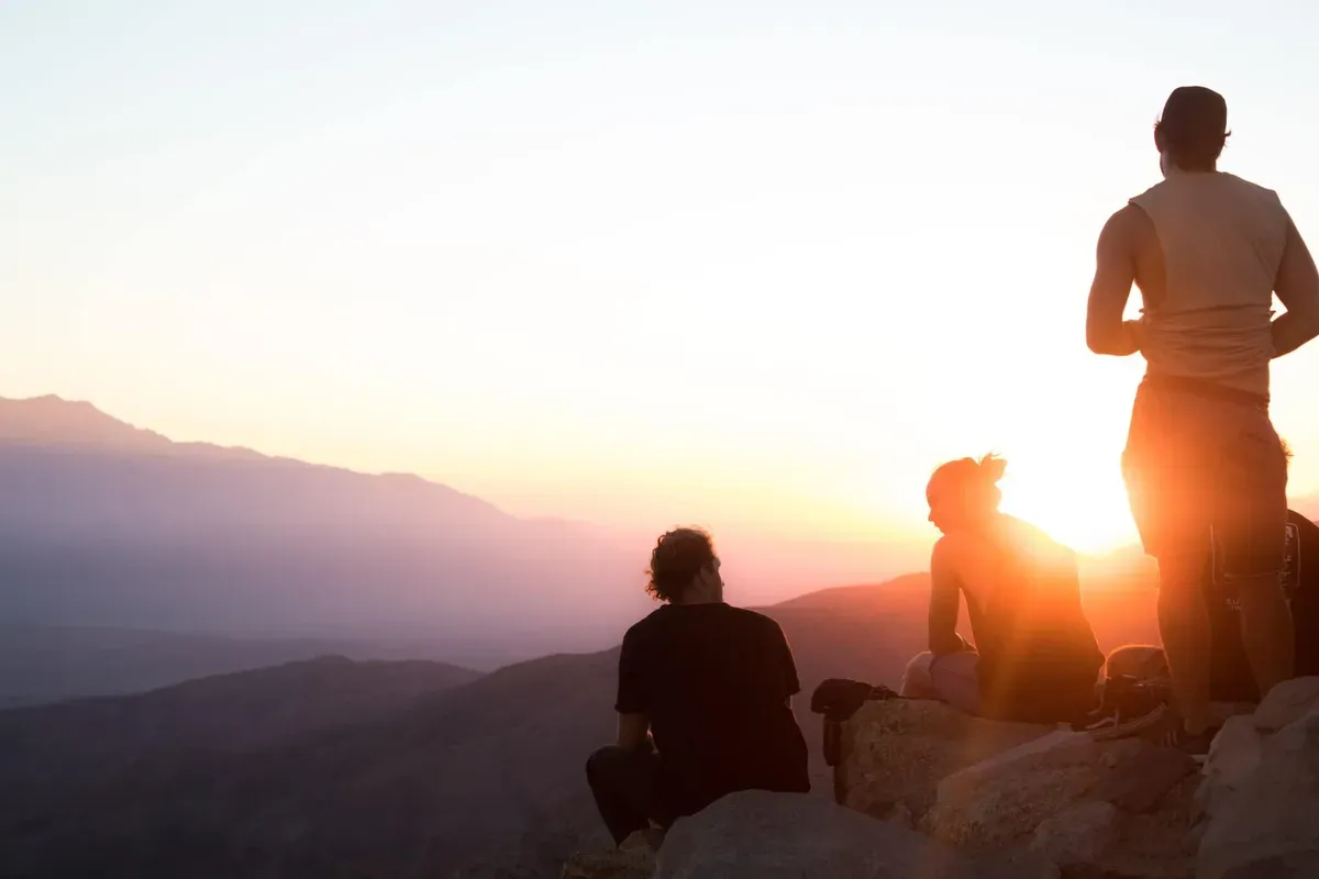Three hikers watching the sunset from a mountain summit