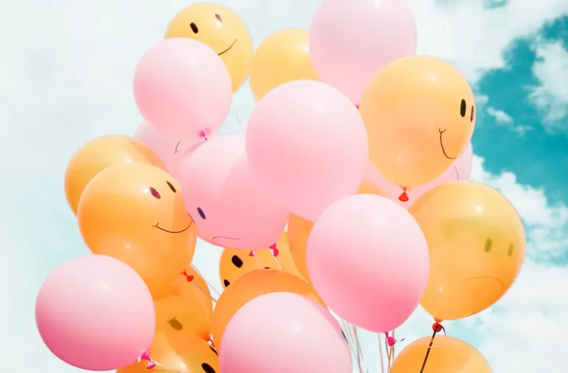 Bunch of pink and yellow balloons with smiley faces against a blue sky