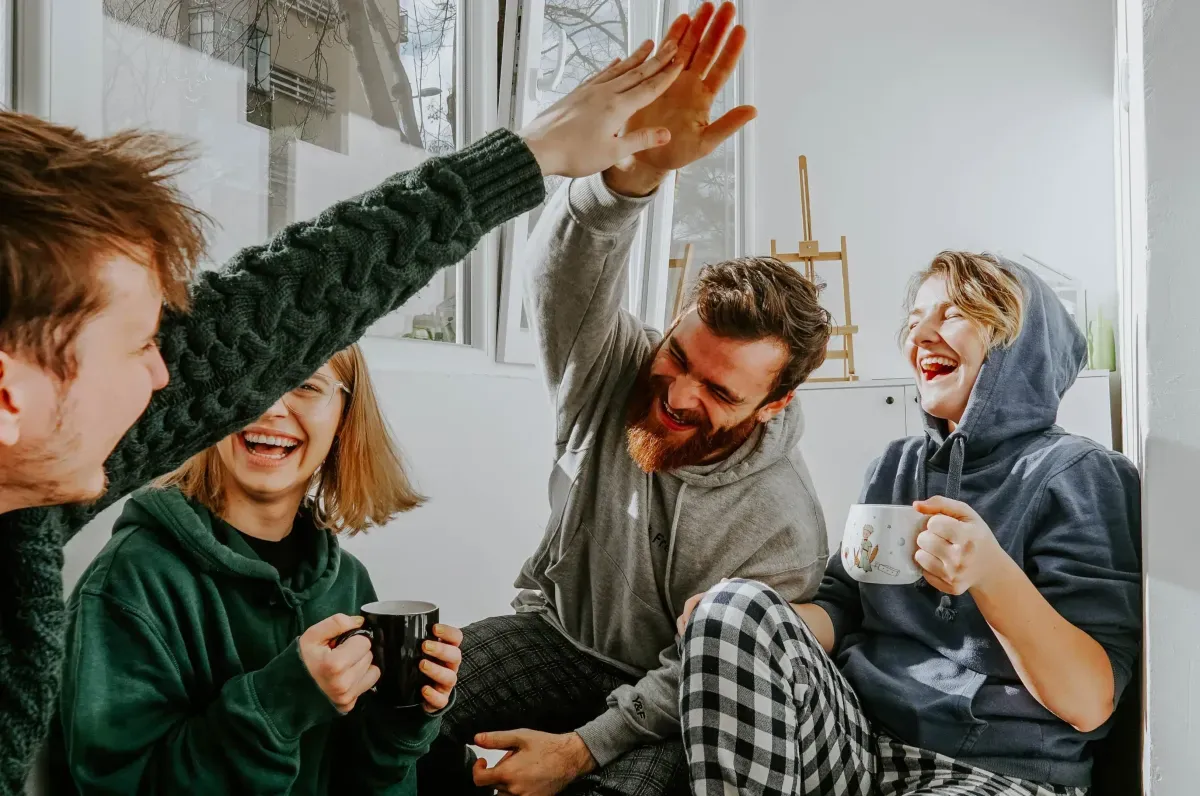 Group of friends laughing and high-fiving while holding coffee mugs