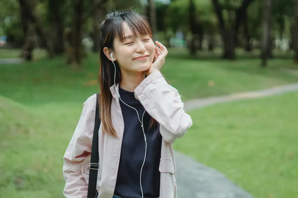 Woman smiling with earbuds in, walking through a park