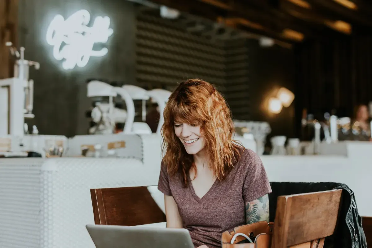 Woman smiling while working on a laptop in a cafe