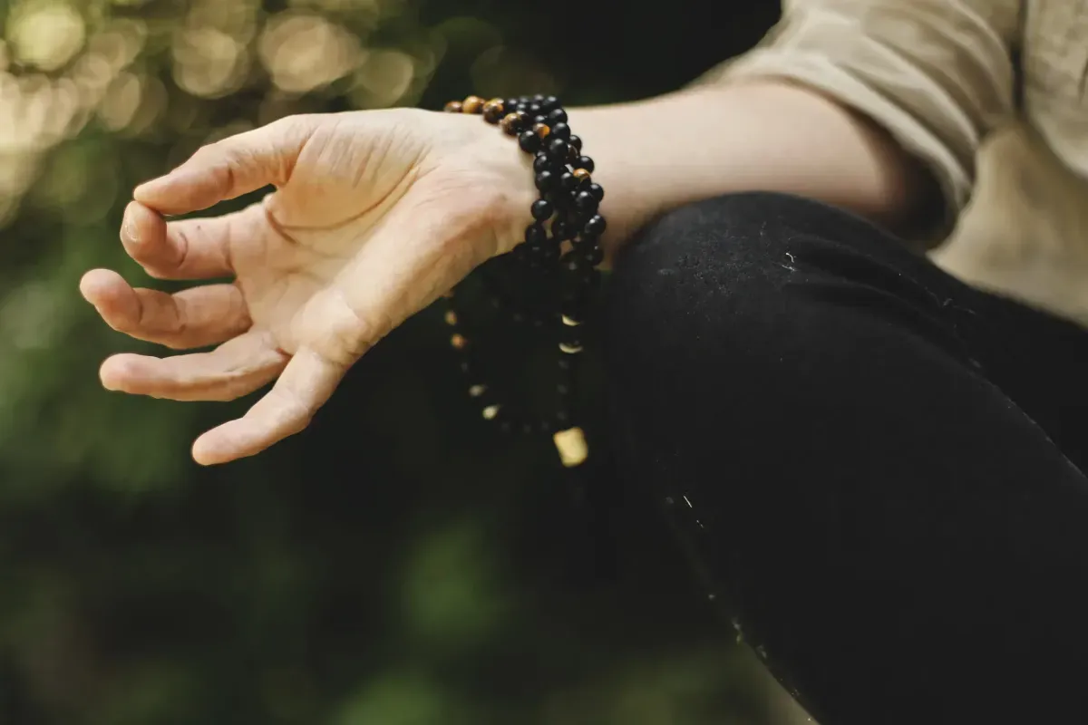 Close-up of a hand wearing mala beads in a meditative pose
