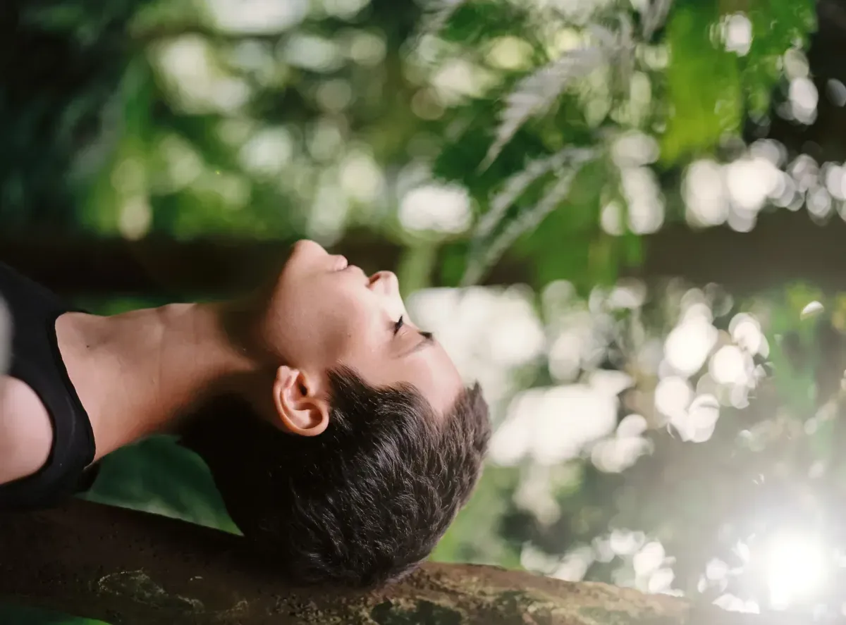Person lying back with eyes closed, relaxing amid greenery