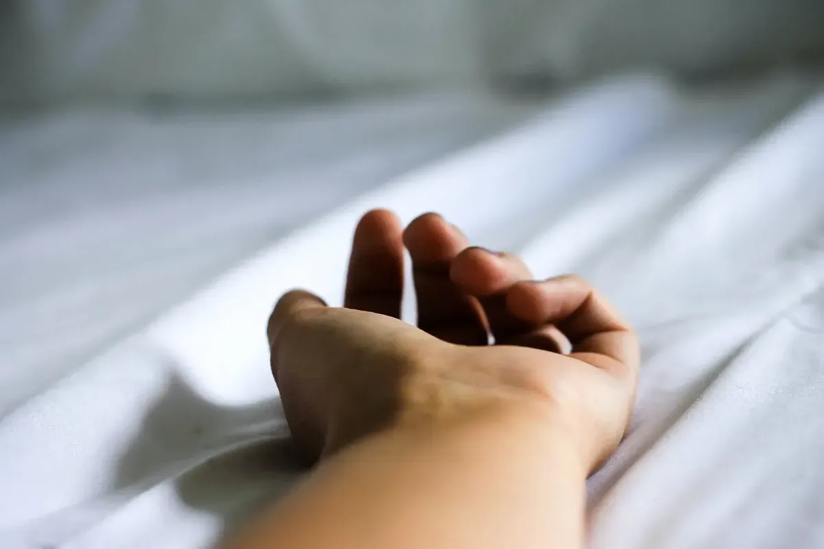Relaxed hand resting open on white bed sheets