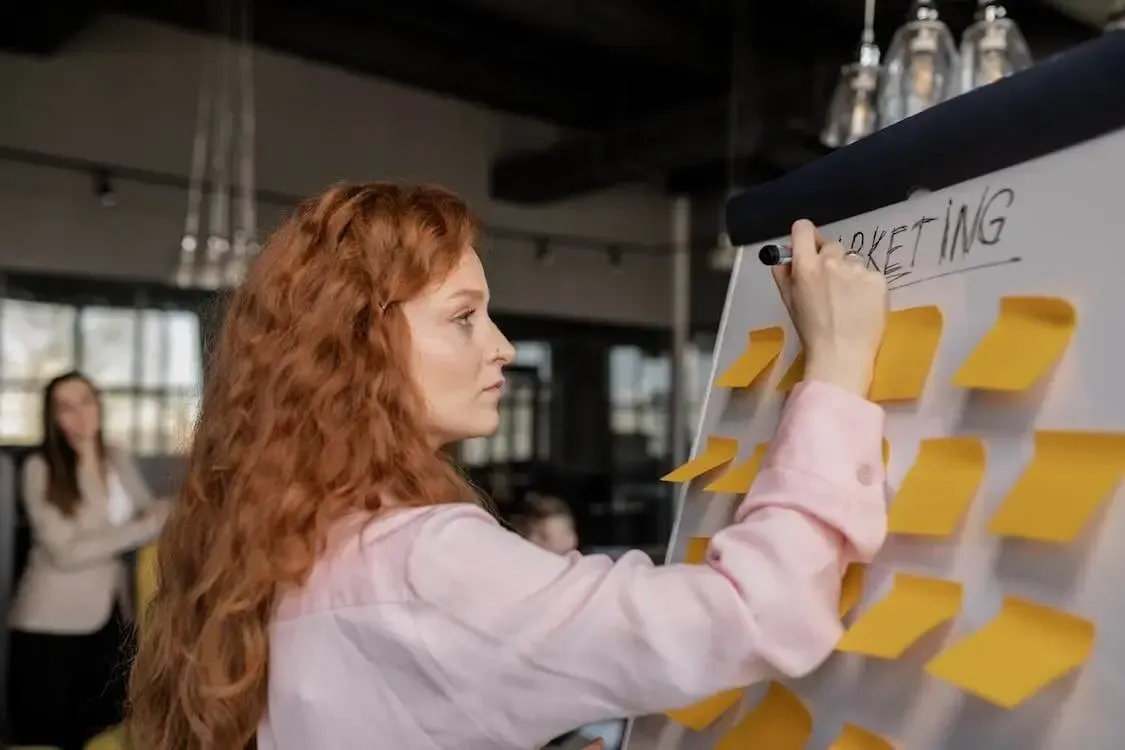 Woman writing on a sticky note board labeled marketing
