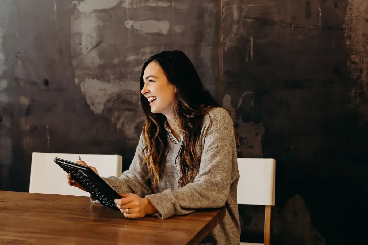 Woman laughing while writing on a tablet at a table