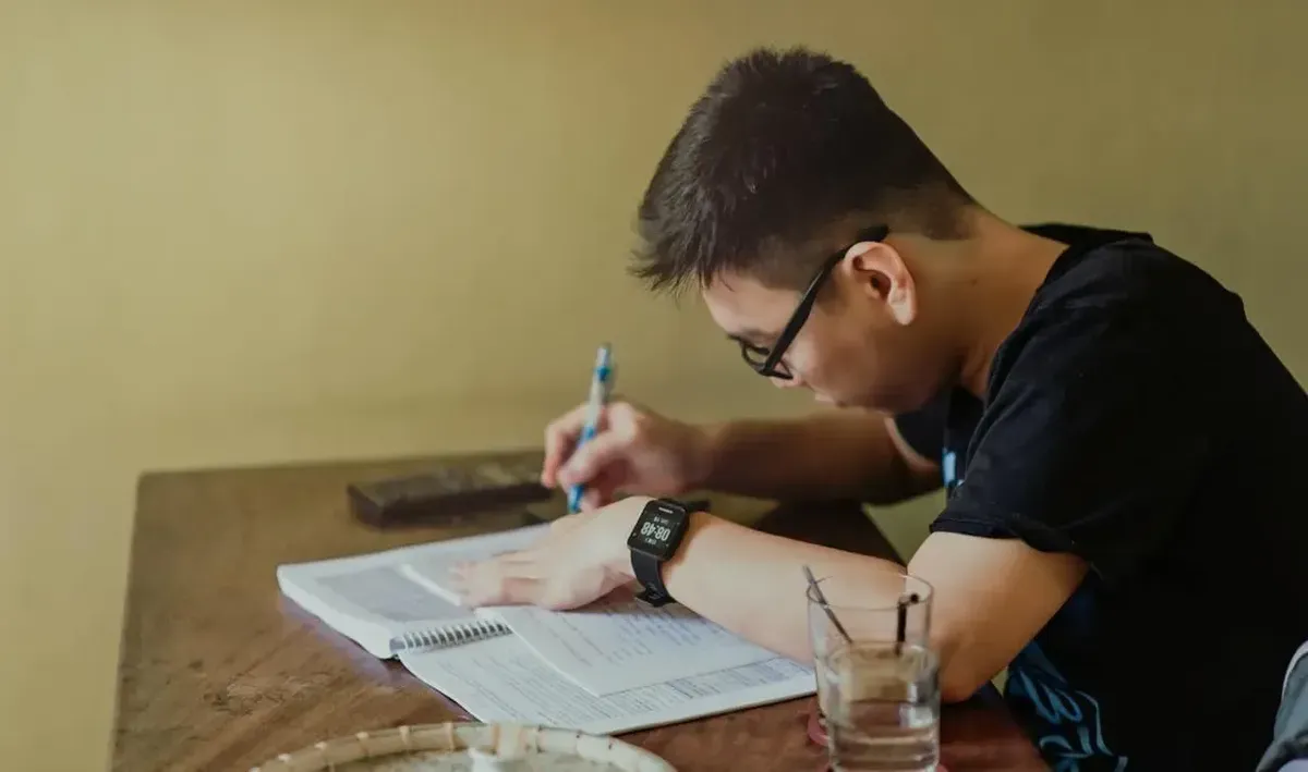 Boy studying at a table while checking his smartwatch