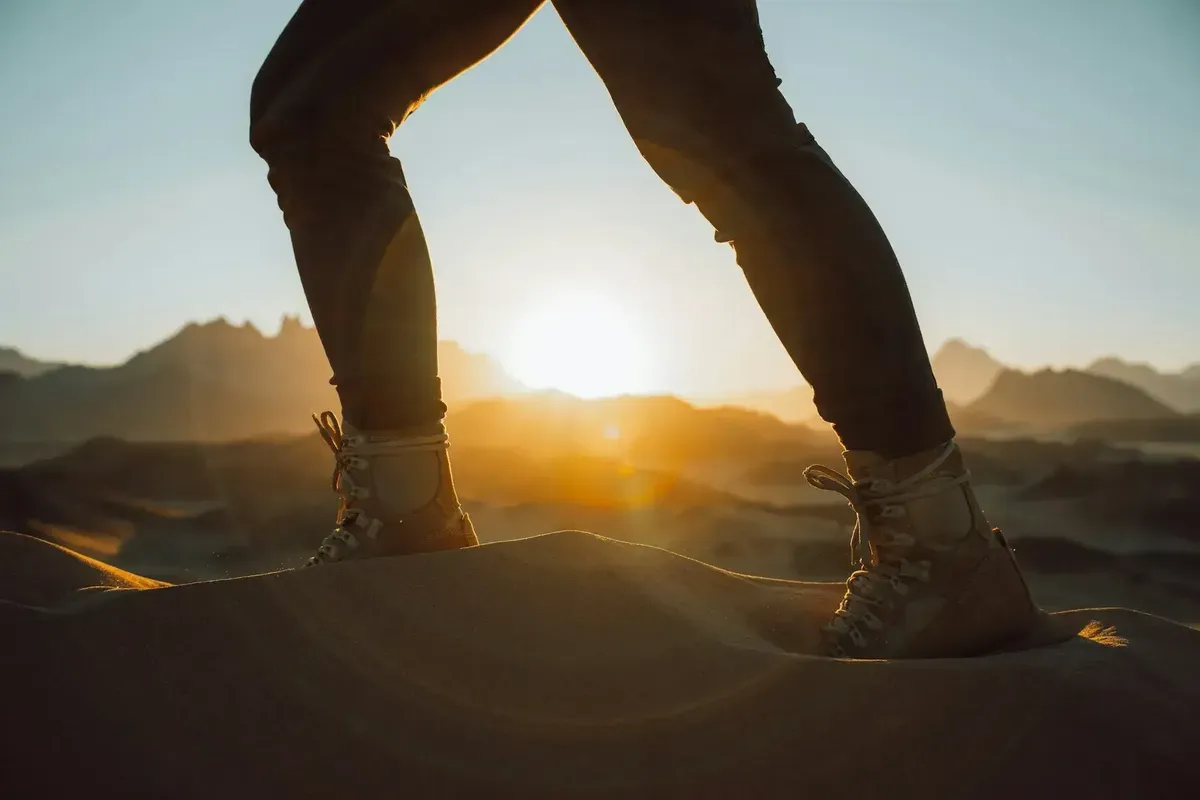 Hiker's boots stepping across a sand dune at sunrise