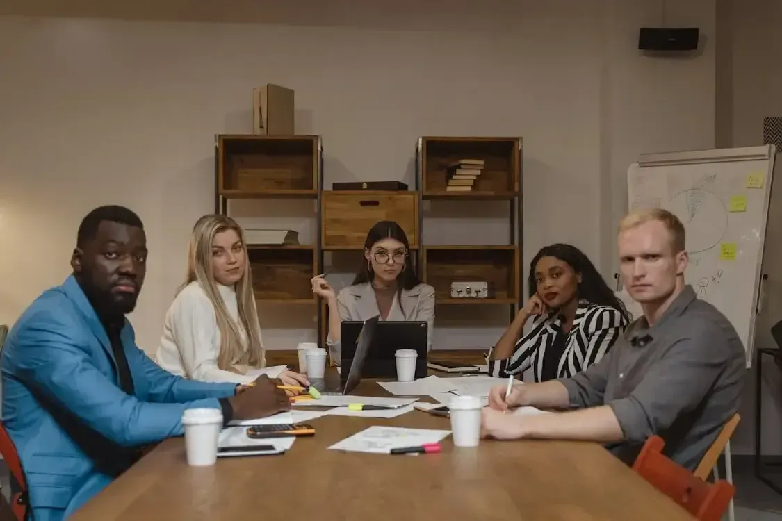 five colleagues sitting around a meeting table looking at the camera