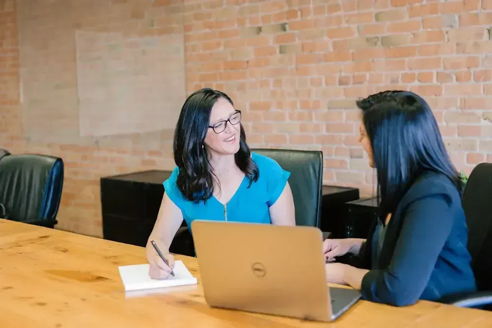 two women talking and taking notes with a laptop open