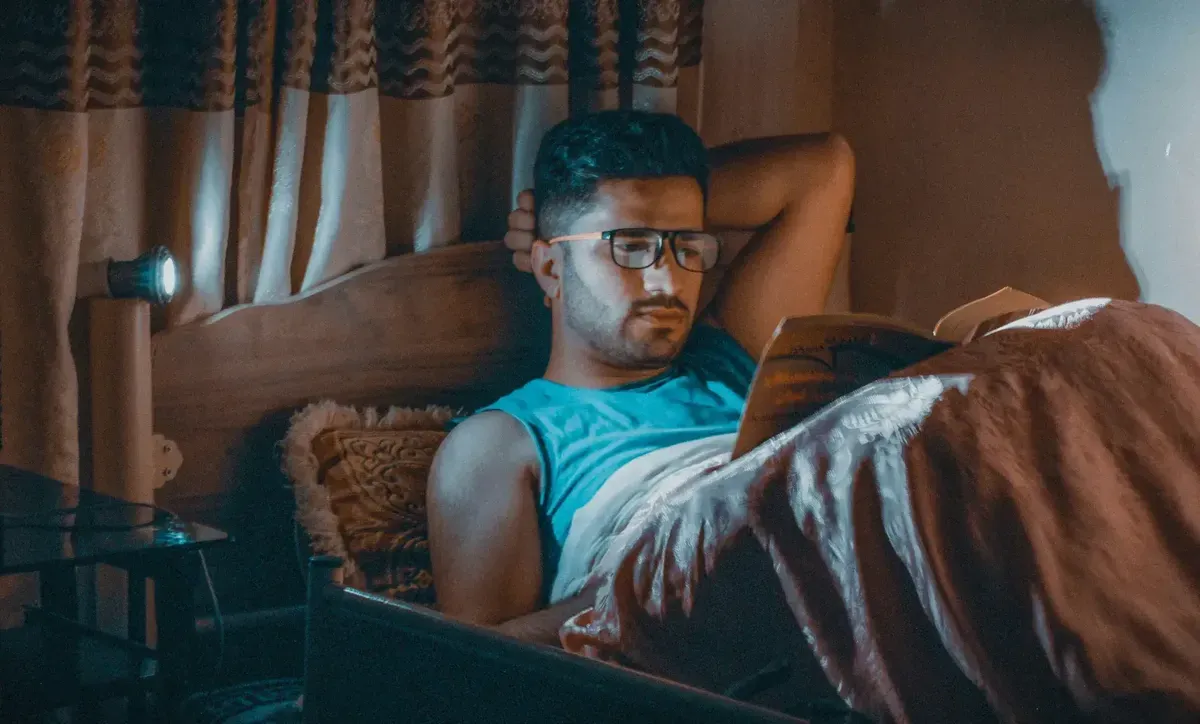 man reading a book in bed at night with a lamp on