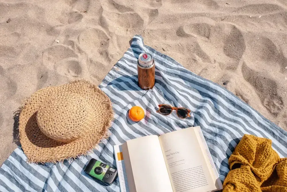 Beach blanket with a straw hat, book, sunglasses and camera