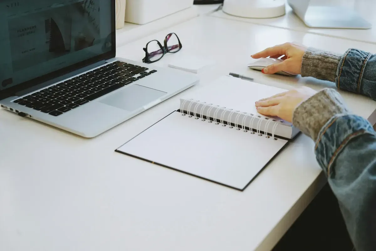 Hands resting on a laptop and blank notebook at a desk