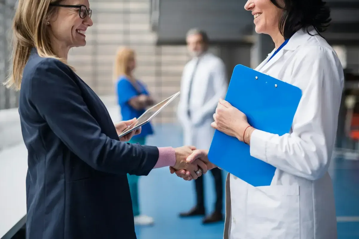Two professional women shaking hands in a clinical workplace setting