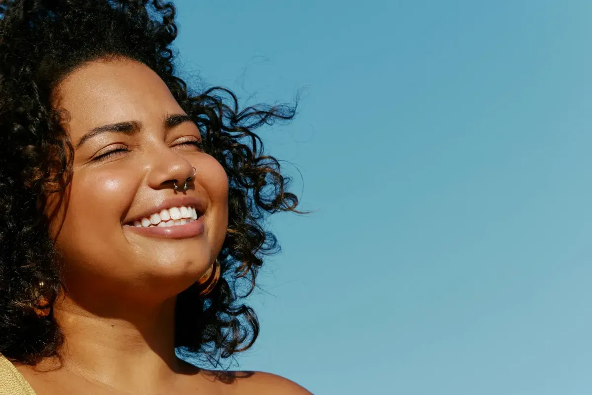 Woman laughing joyfully with her eyes closed against a blue sky