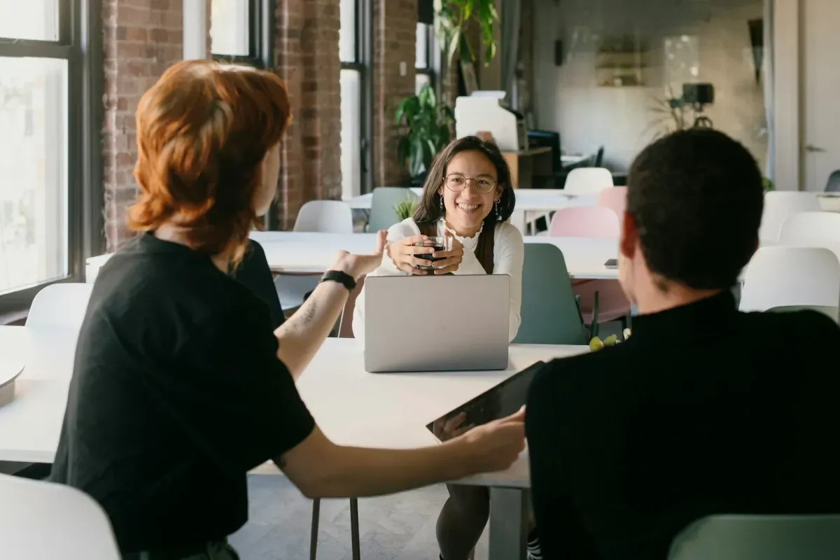 three coworkers chatting around a laptop in a bright office