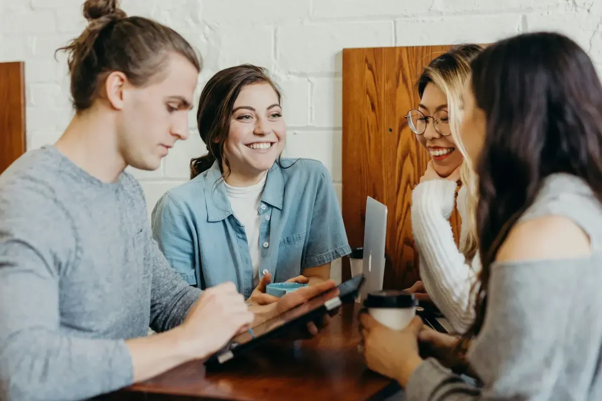 four friends laughing together over coffee and a laptop